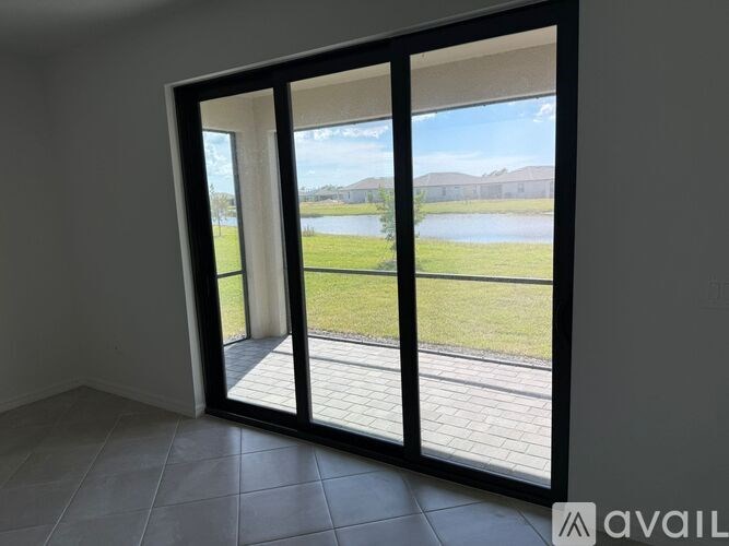 A room with a sliding glass door leading to a patio with a view of a lake and houses.