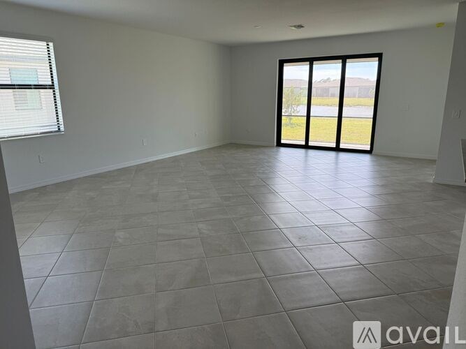 A spacious room with tiled flooring and a view of a grassy area through the sliding glass door.