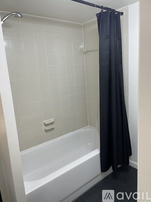 A bathroom with a white tub and a black shower curtain.