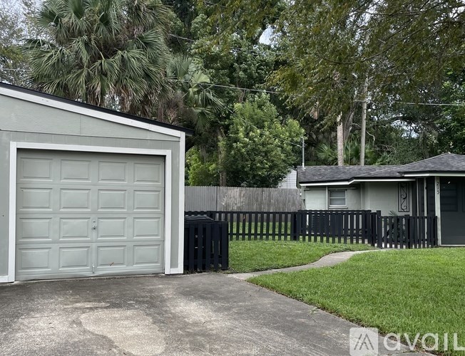 A white garage door is on the left of a house with a black fence.
