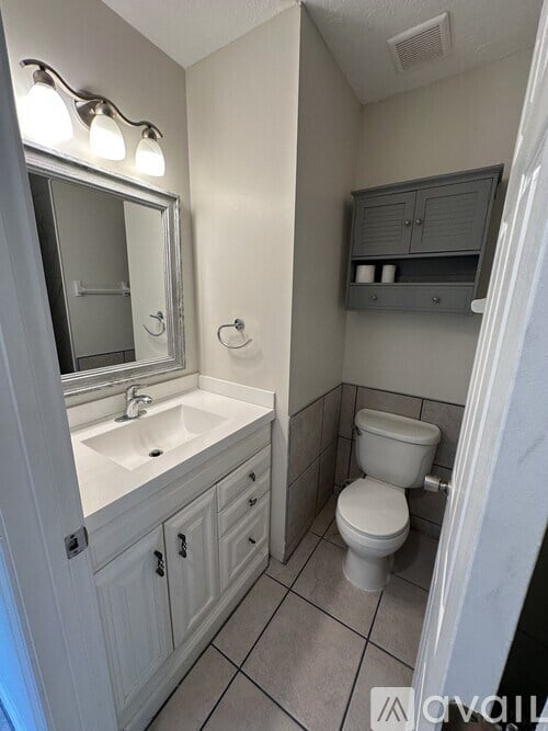A bathroom with a toilet, sink, and mirror.