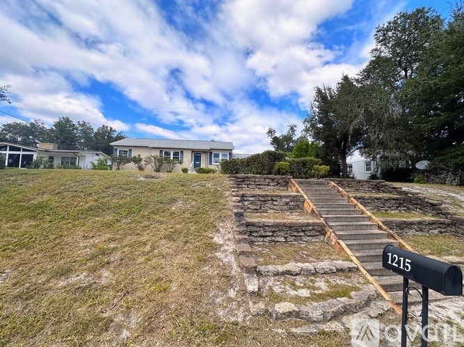 A sign with the number 1215 is in the foreground of a grassy area with a pathway leading to a building.