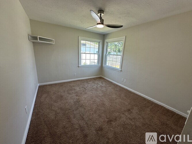 A room with a carpeted floor, a ceiling fan, and two windows.