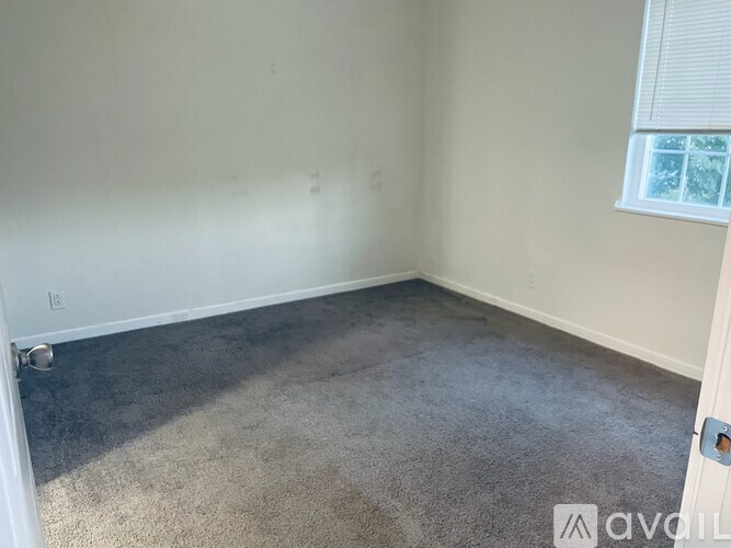 A room with a carpeted floor and a window with blinds.