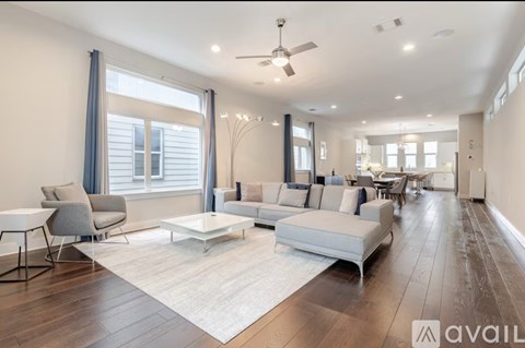 A spacious living room with a white sofa set and a wooden floor.