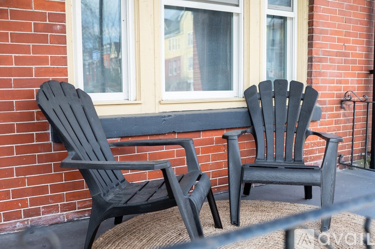 Two black chairs and a bench on a porch.