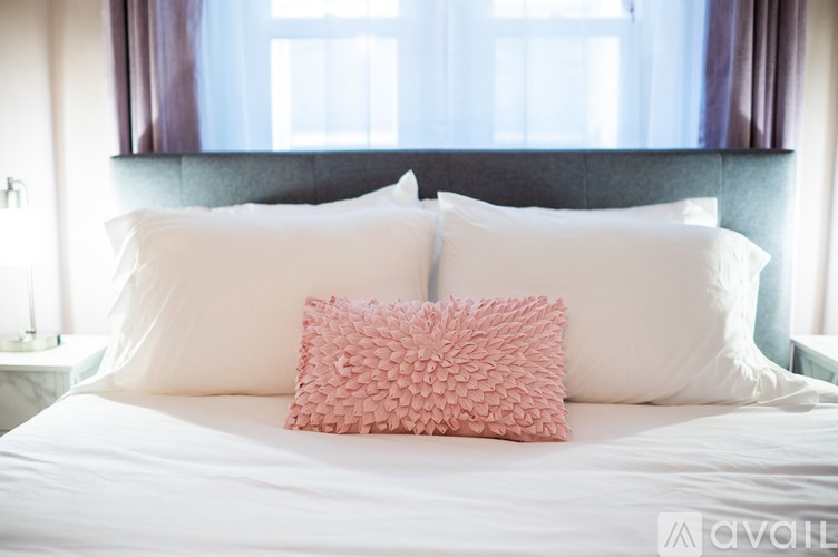 A bed with white pillows and a pink pillow with a leaf pattern in the middle.