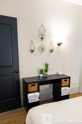 A black door is on the left of a white wall with three green plants on a black table.