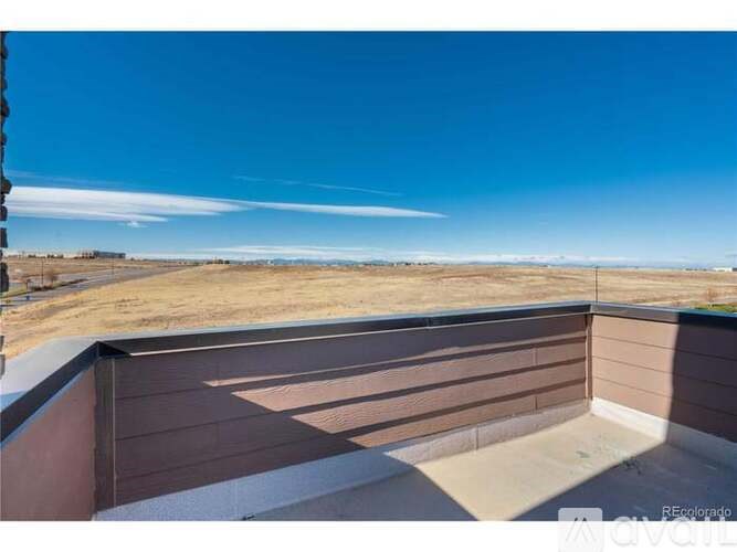 A balcony with a wooden railing overlooking a dry, grassy landscape under a clear blue sky.