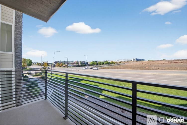 A balcony with a metal railing overlooks a parking lot and distant buildings.