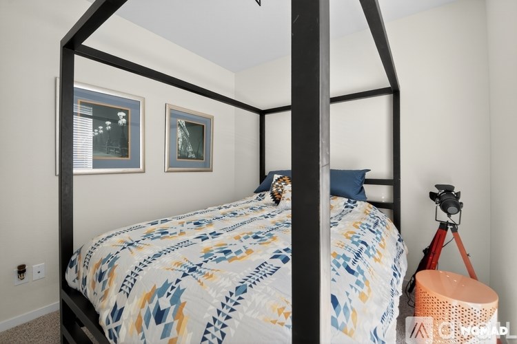 A bed with a blue and yellow comforter sits in a room with a camera on a tripod.