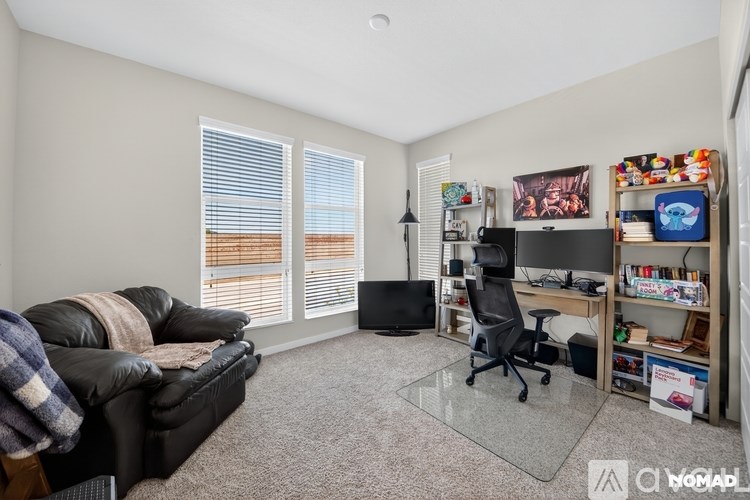 A living room with a black couch, a desk with a computer, and a bookshelf filled with various items.