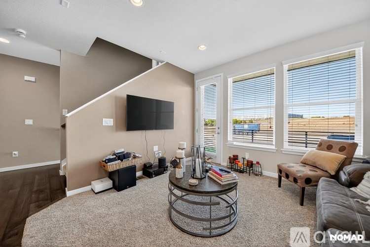 A living room with a brown couch, a coffee table, and a flat-screen TV mounted on the wall.