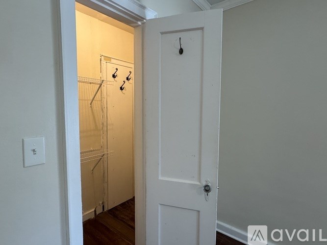 A white door with a black handle is open to a hallway with a coat rack.