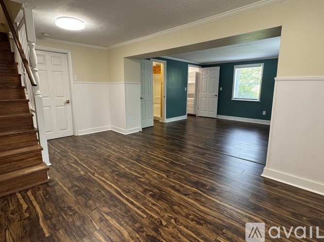 A spacious room with wooden flooring and a staircase on the left side.