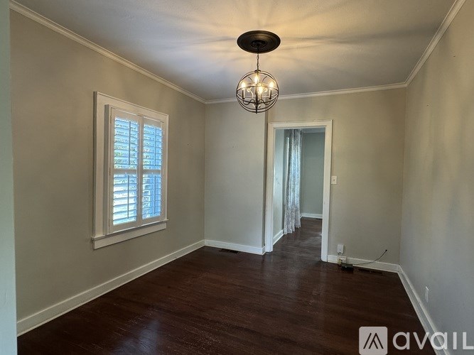 A room with a chandelier, a window with blinds, and a door with a curtain.