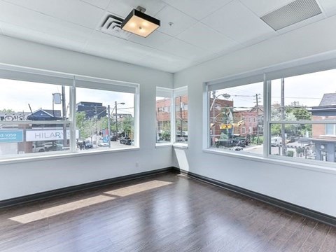 A room with white walls and wooden flooring, with windows showing a view of a street with cars and buildings.