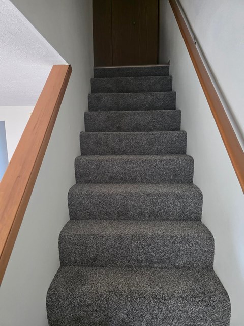 A staircase with a grey carpeted runner and wooden handrails.