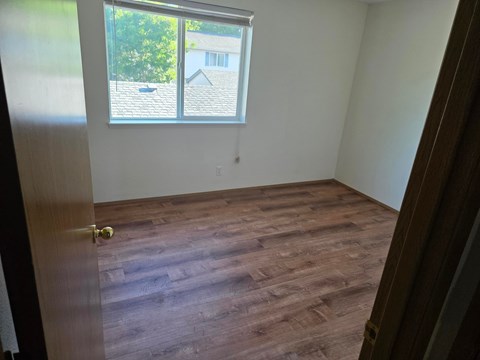 A room with a wooden floor and a window showing a house and trees outside.