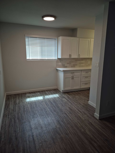 A kitchen with white cabinets and a window with blinds.