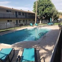 A pool with lounge chairs and a fence in front of a building.