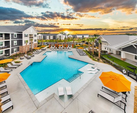 A large swimming pool surrounded by lounge chairs and umbrellas at dusk.