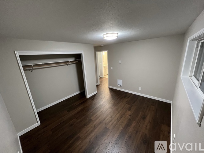 A room with a wooden floor and a white wall with a window.