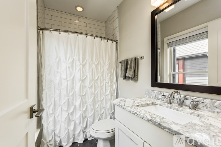 A white bathroom with a marble counter top and a shower with a white curtain.