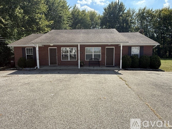 A small brick house with a porch and a driveway in front.