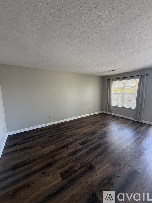 A room with wooden flooring and a window with grey curtains.