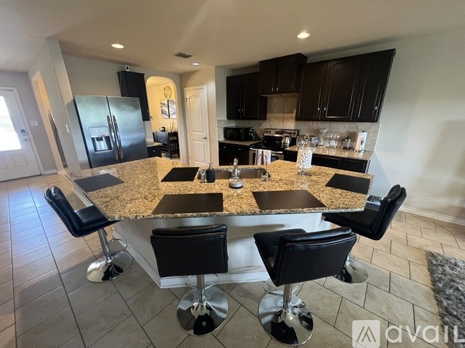 A kitchen with granite countertops and black chairs.