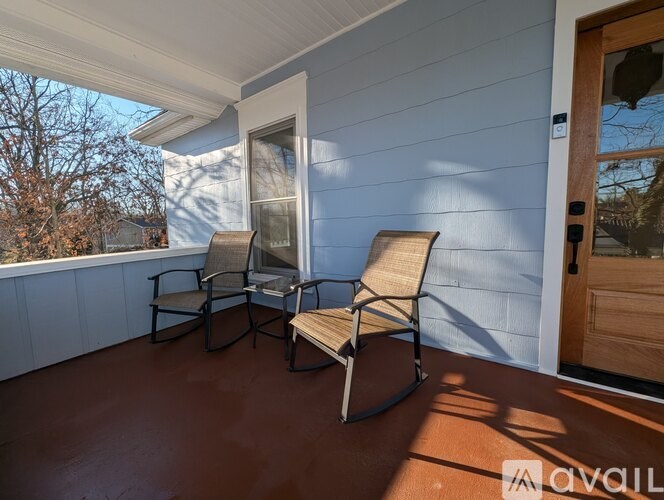 Two chairs are on a porch with a white wall and a door.