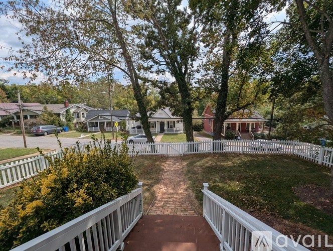 A white picket fence surrounds a brick pathway in a residential area.