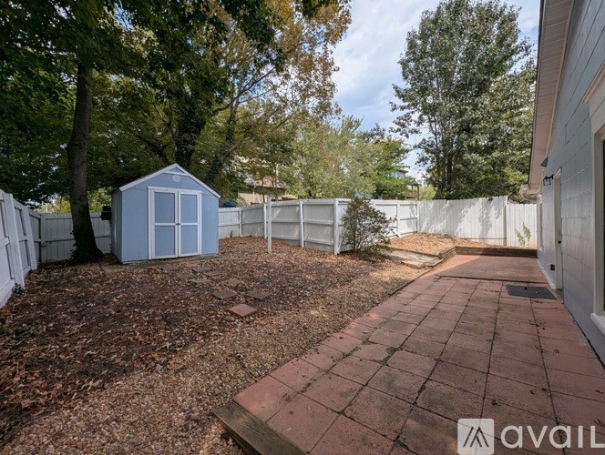 A backyard with a blue shed, a brick walkway, and a white fence.
