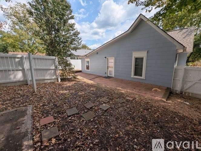 A small grey house with a white fence and a gravel yard.