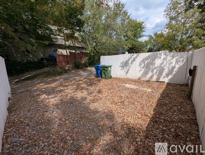 A backyard with a white fence and a blue barrel.
