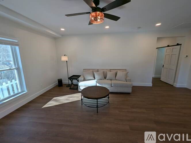 A living room with a white couch, a brown table, and a ceiling fan.