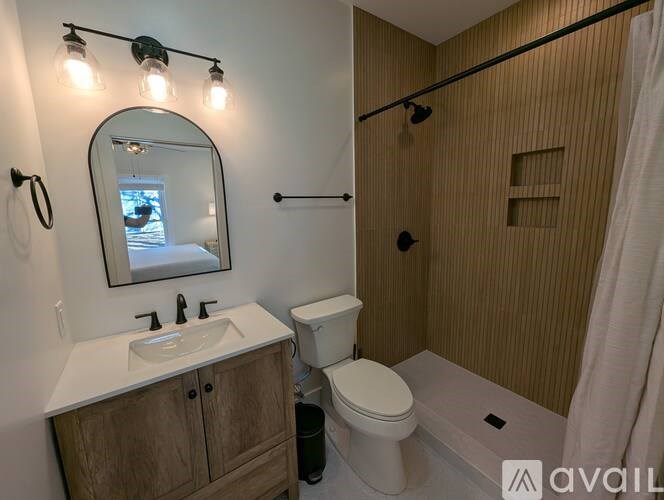 A bathroom with a toilet, sink, mirror, and shower.