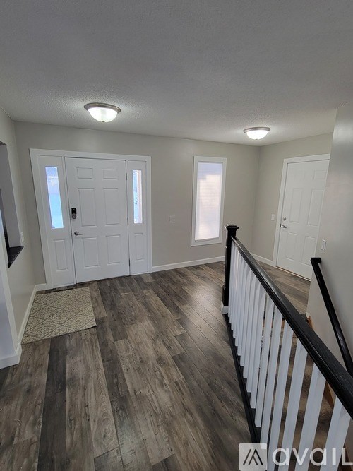 A room with wooden floors and white walls, with a black railing on the right side.