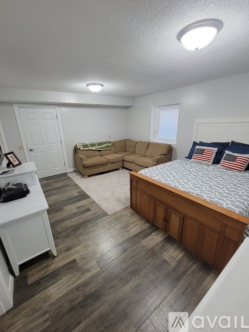 A bedroom with a bed, couch, and a wooden floor.