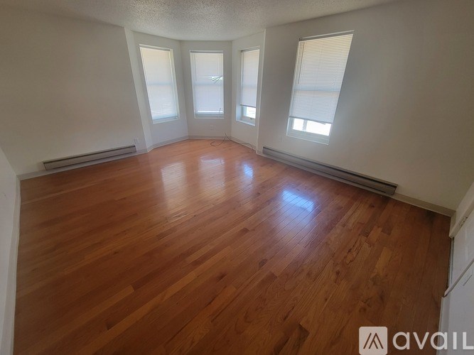 A room with wooden flooring and three windows.