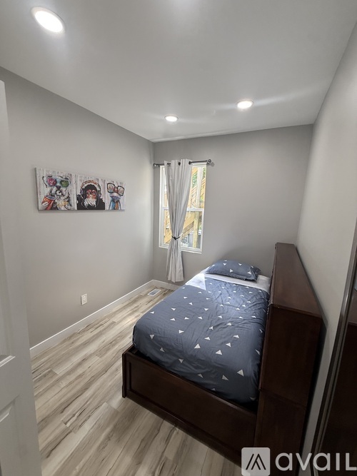 A bedroom with a bed, wooden floors, and a window with curtains.
