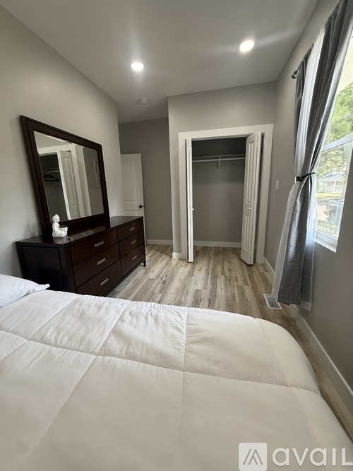 A bedroom with a large bed, a dresser with a mirror, and a sliding glass door leading to a balcony.