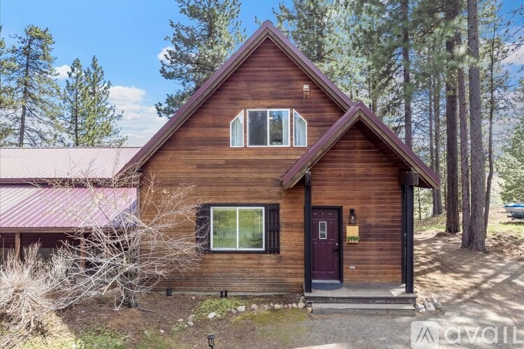 A brown wooden cabin with a red door and windows surrounded by trees.