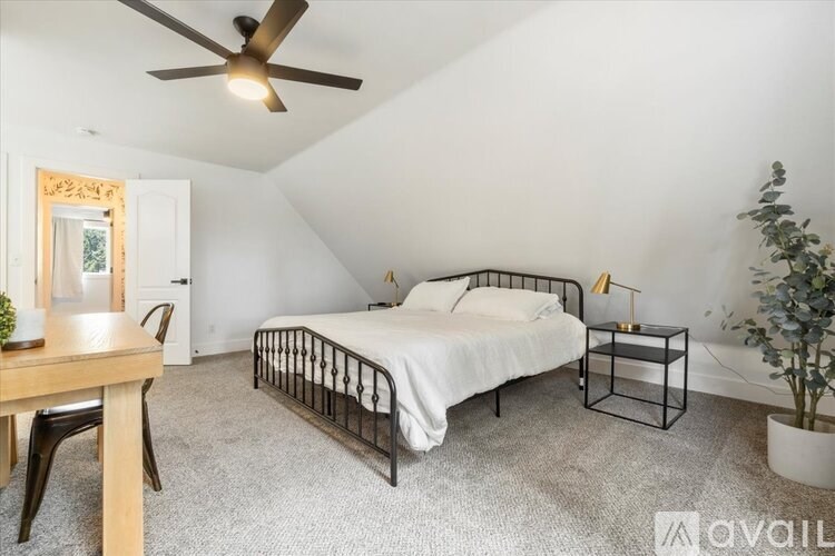 A bedroom with a bed, a chair, a table, and a ceiling fan.