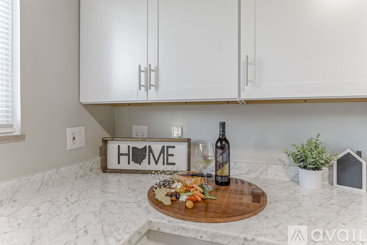 A wooden cutting board with food and a bottle of wine on a marble countertop.
