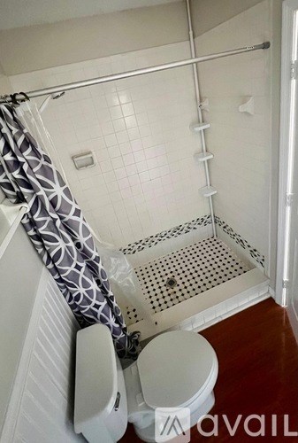 A bathroom with a toilet, a shower with a curtain, and a tiled floor.