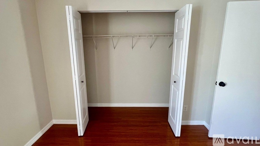 A white closet with a wooden floor and a black door handle.