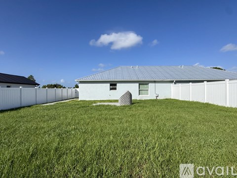 A large white building with a grey roof is surrounded by a grassy field.