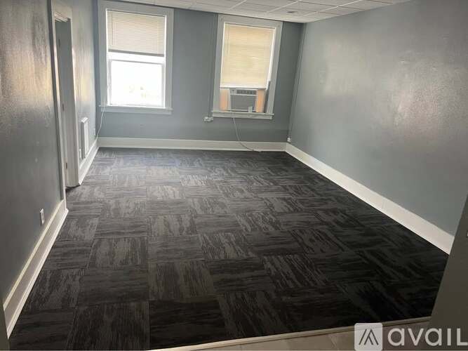 A room with a carpeted floor and two windows.